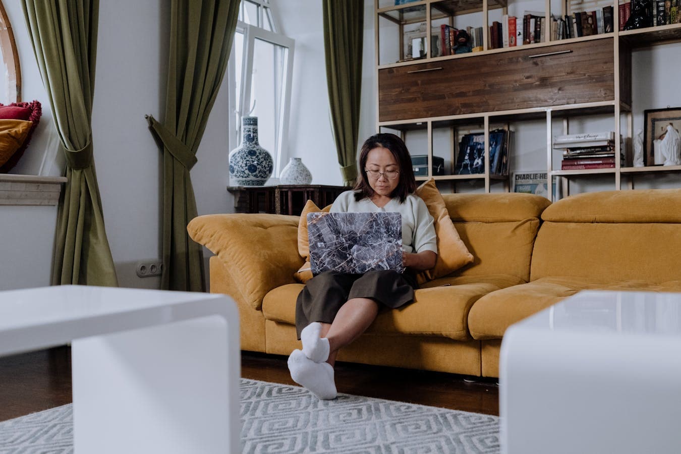 A woman sits on her couch in a quiet living room during an online therapy session on her laptop.