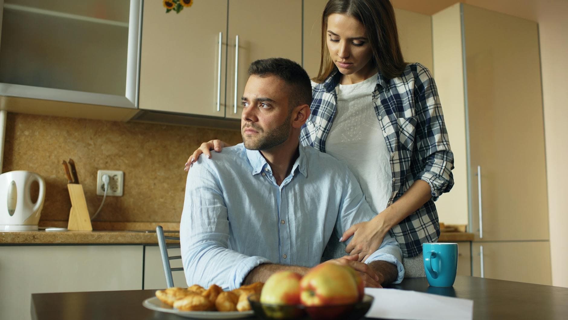 A couple sitting together in a quiet kitchen, sharing a thoughtful and emotional moment.