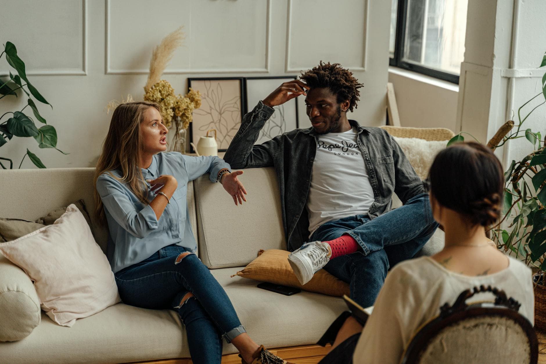 A woman speaks during a couples therapy session while a therapist listens and takes notes.