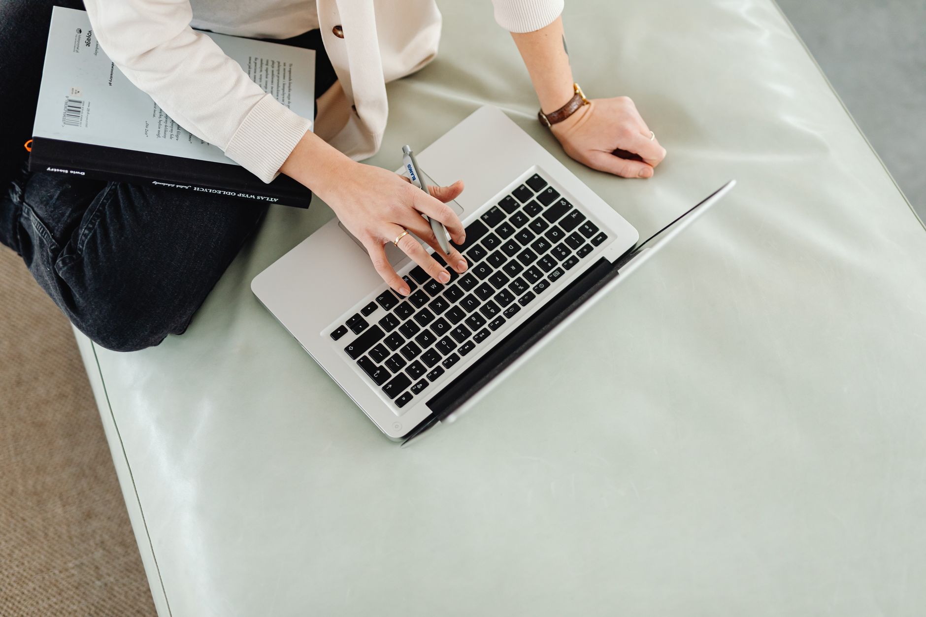 A person works on a laptop with a notebook and pen nearby.