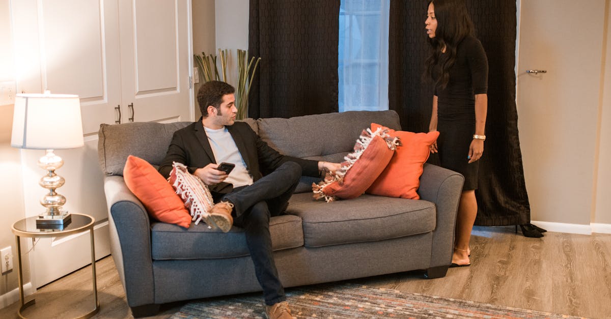 A couple sits at a kitchen table, one person speaking while the other looks away with arms crossed, mid-argument.