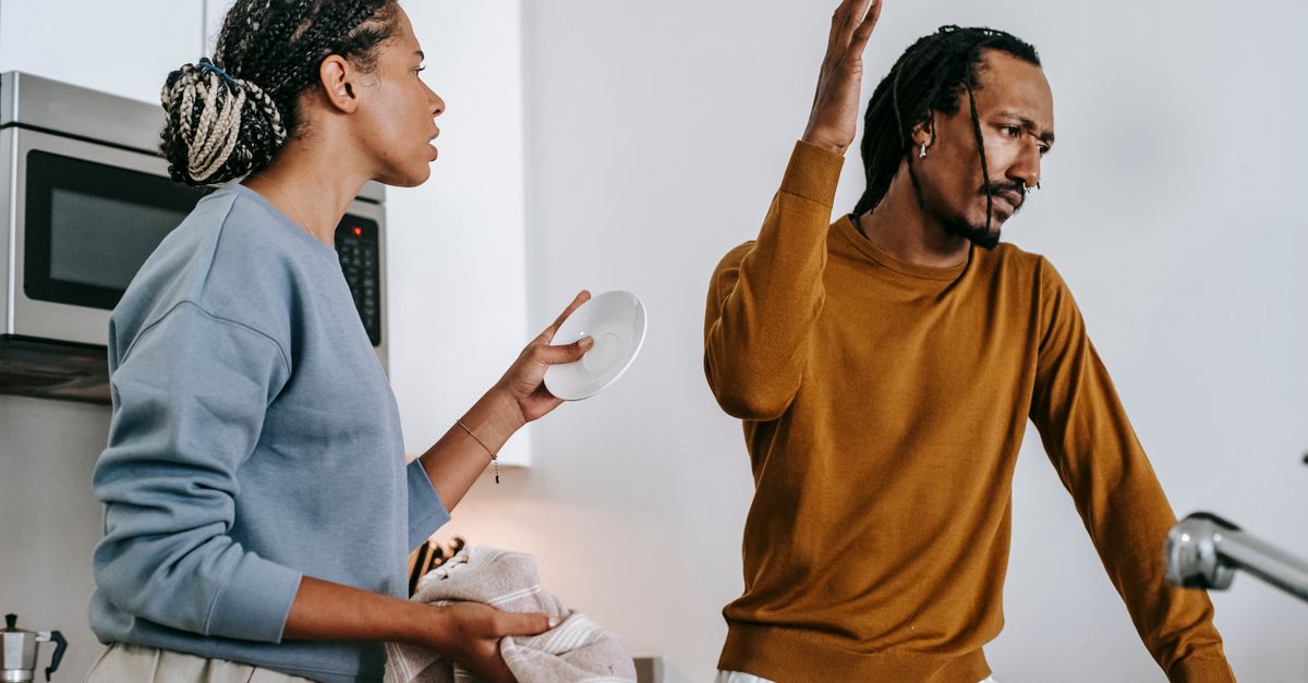 A couple in a kitchen in the middle of a tense argument, with the man turning away with a raised hand while the woman tries to talk to him.