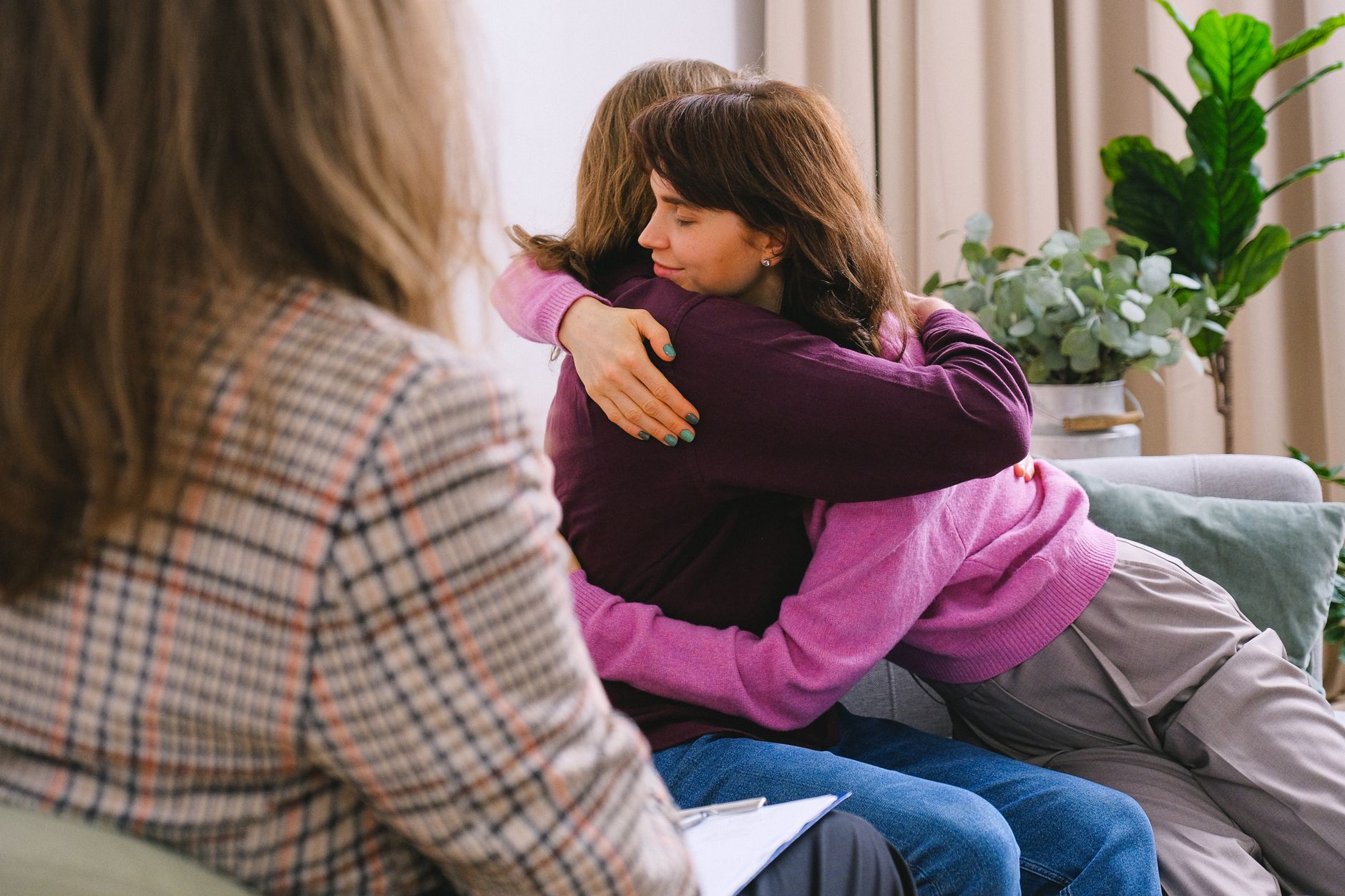 Side view of couple sitting on sofa and embracing during session with psychologist in light room in daytime.